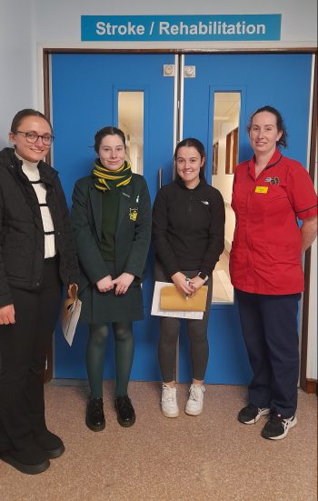 Four females standing smiling outside a door with a sign for Stroke/ Rehabilitation