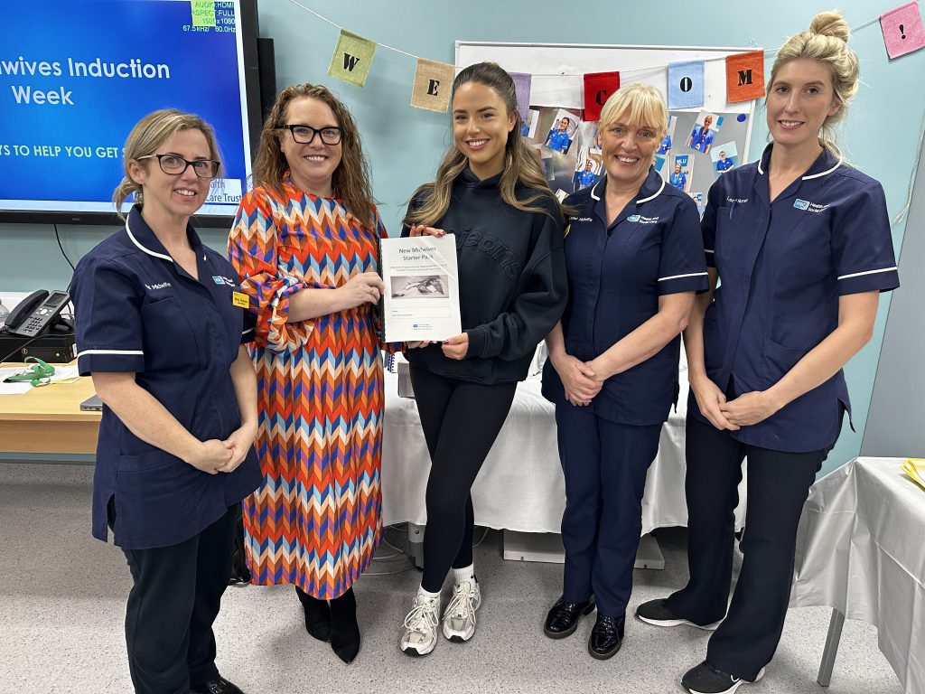 Two women both holding a booklet alongside three lead midwives in uniform