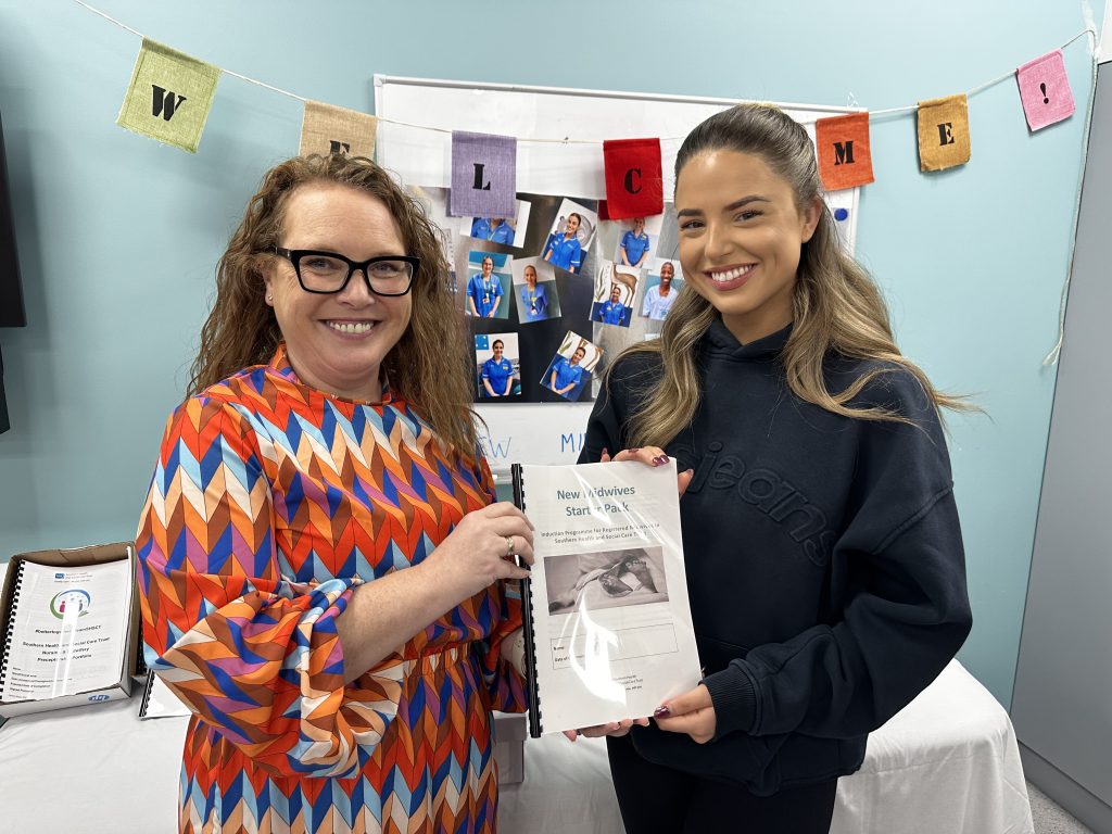 Two midwives, not in uniform, holding an induction booklet