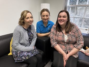 Three women sitting on sofa looking at camera