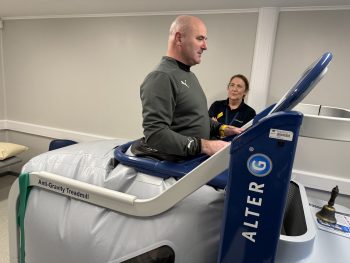 Man on standing in anti-gravity treadmill with woman physio to his right