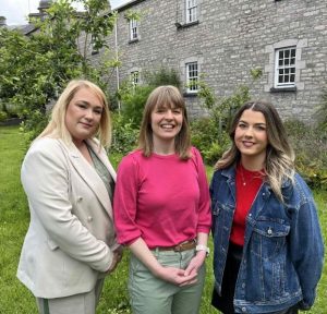 Three women stand outside an old building posing for the camera.